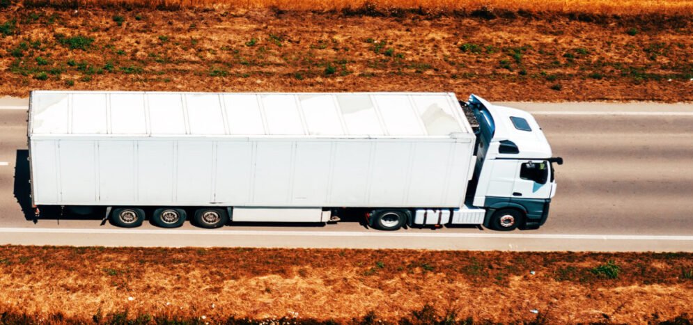 White truck on highway through countryside landscape, aerial sho